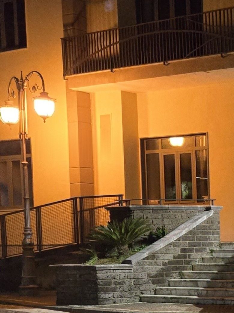 Facciata di un municipio illuminata dal vecchio lampione a luce gialla, prima dell'intervento